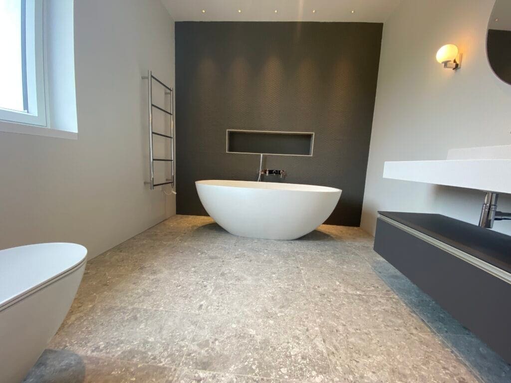 Planning Plumbing and Heating for Kitchen, Utility and Extension Projects in Mulbarton | Allstar Systems Ltd Luxury bathroom with freestanding white bath, dark feature wall, stone-effect floor tiles and wall-mounted basin