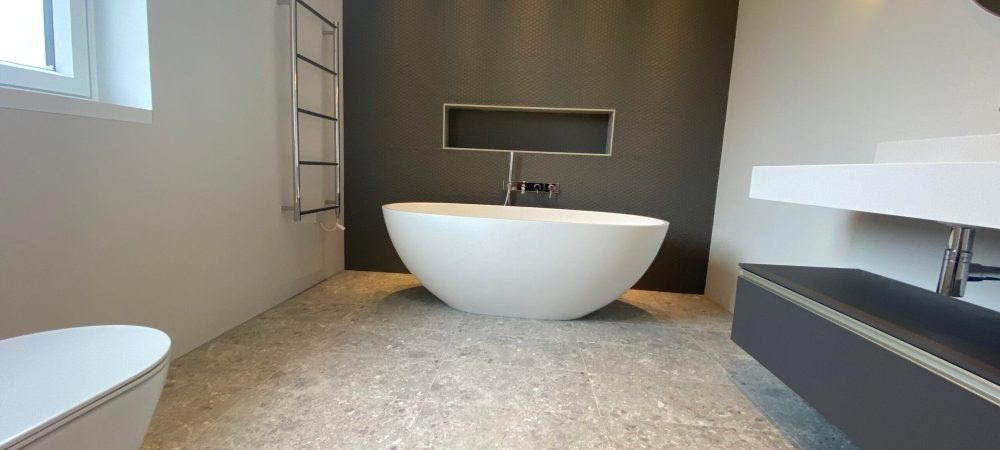 Luxury bathroom with freestanding white bath, dark feature wall, stone-effect floor tiles and wall-mounted basin