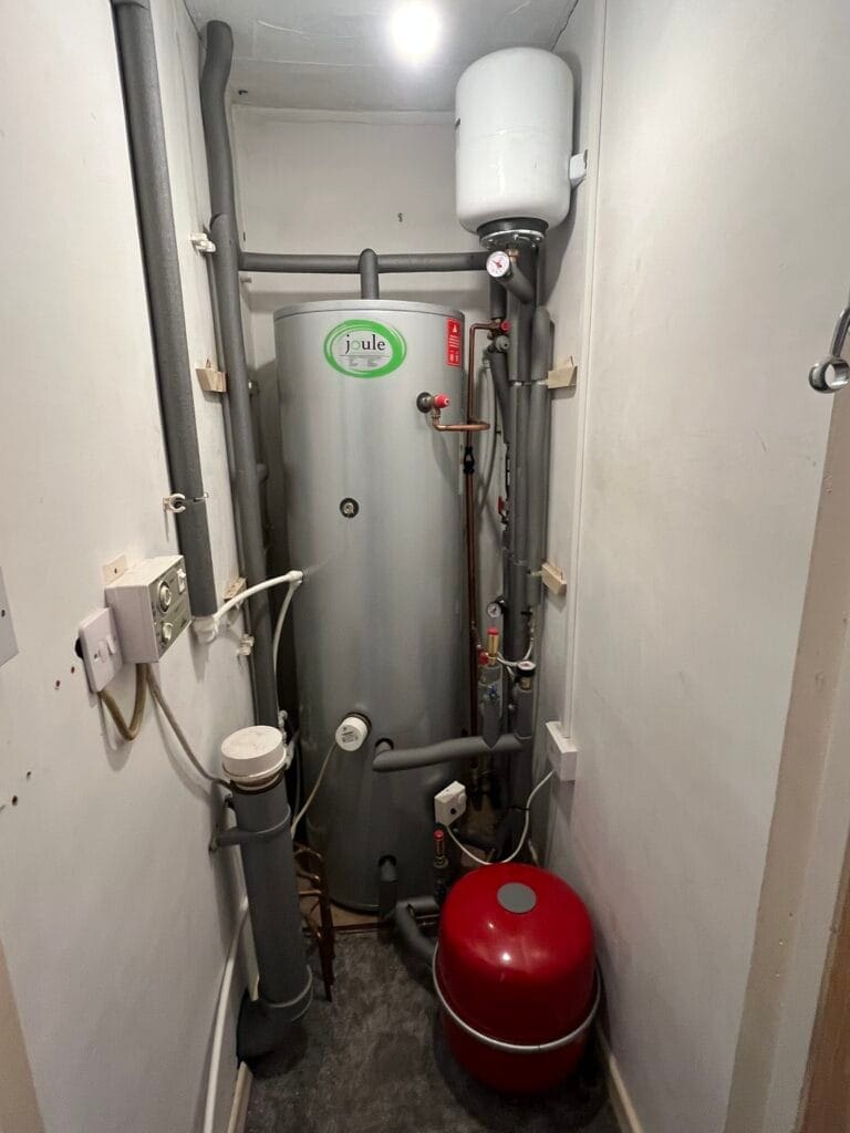 Hot water cylinder with expansion vessel, pipework and heating controls in a domestic airing cupboard